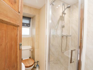 A bathroom with a wooden door toilet with wooden seat and a glass shower enclosure at Above Deck in Beaumaris