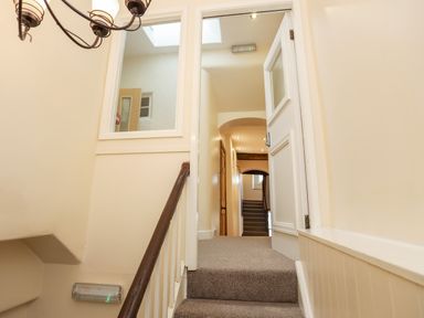 A stairway with carpet leading to a hallway with wooden doors and recessed ceiling lights at Above Deck in Beaumaris