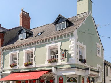 A two storey building with a green facade and white window frames with flower boxes at Above Deck in Beaumaris