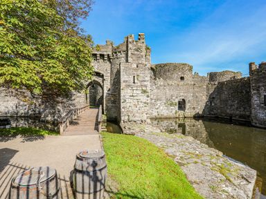 A stone castle with a wooden bridge over a moat and barrels on the grass at Above Deck in Beaumaris
