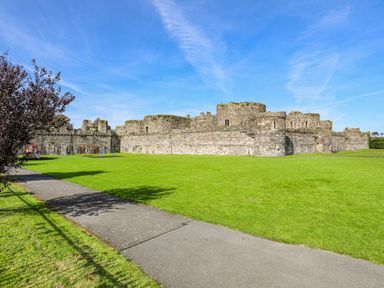 A grassy park area with a paved walkway and a stone castle wall in the background at Above Deck in Beaumaris
