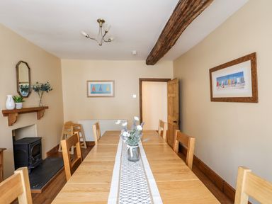 A dining room with a long wooden table and chairs a vase with flowers on the table a fireplace with mantle and decorative items two framed pictures on the walls and a wooden beam on the ceiling at Above Deck in Beaumaris