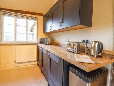 A kitchen with a wooden countertop dark cabinets a microwave toaster kettle and a window at The Abbey Cottage in Windsor Green