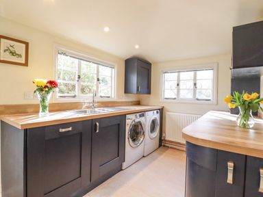 A utility room with washer and dryer under wooden countertops and flowers in vases at The Abbey Cottage in Windsor Green