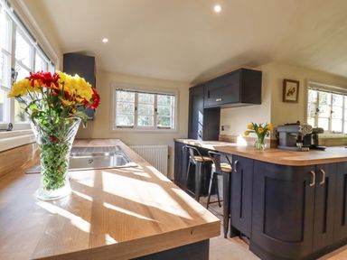 A kitchen with wooden countertops flowers in vases and black cabinets at The Abbey Cottage in Windsor Green