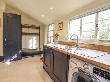 A utility room with a washing machine sink window and storage cabinets at The Abbey Cottage in Windsor Green