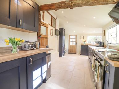 A kitchen with dark cabinets wooden countertops a toaster a kettle flowers and a stove at The Abbey Cottage in Windsor Green