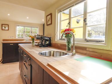 A kitchen with wooden countertops a stainless steel sink coffee machine and flowers by the window at The Abbey Cottage in Windsor Green