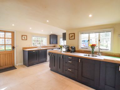 A kitchen with dark cabinets wooden countertops two windows a sink coffee machines and a wooden door at The Abbey Cottage in Windsor Green