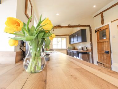 A kitchen with a wooden countertop and a vase of yellow tulips at The Abbey Cottage in Windsor Green