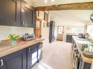 A kitchen with dark cabinets wooden countertops a toaster kettle flowers and a wooden door at The Abbey Cottage in Windsor Green