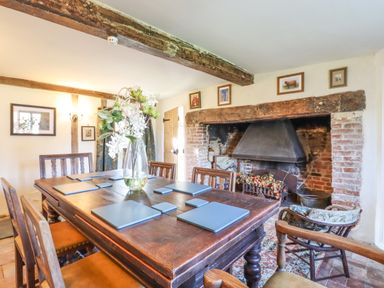 A dining room with a wooden table and chairs a large fireplace and floral decoration at The Abbey Cottage in Windsor Green