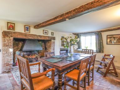 A dining room with wooden table and chairs stone floor and a large brick fireplace at The Abbey Cottage in Windsor Green