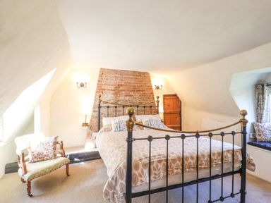 A bedroom with a metal framed bed a patterned bedspread a small armchair and a window seat with cushions at The Abbey Cottage in Windsor Green