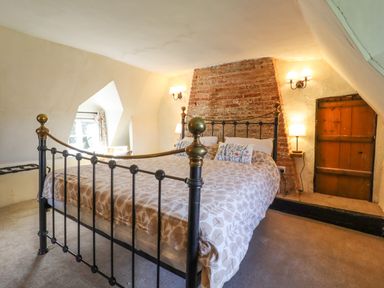 A bedroom with a metal bed frame, patterned duvet, lamps, and exposed brick wall at The Abbey Cottage in Windsor Green