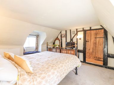 A bedroom with a bed a wooden dresser a mirror a window seat and a wooden door at The Abbey Cottage in Windsor Green