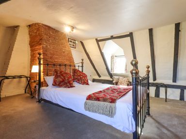 A bedroom with a metal bed frame and red cushions next to a brick chimney breast at The Abbey Cottage in Windsor Green