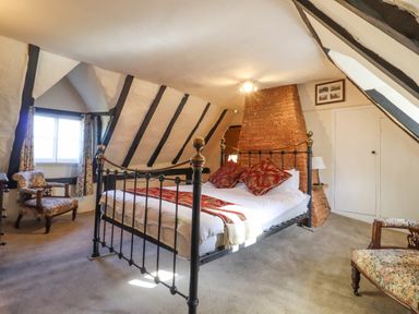 A bedroom with a metal bed frame two armchairs and a brick chimney at The Abbey Cottage in Windsor Green