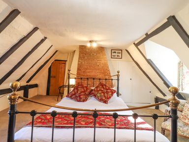 A bedroom with a metal bed frame red cushions and a brick chimney at The Abbey Cottage in Windsor Green