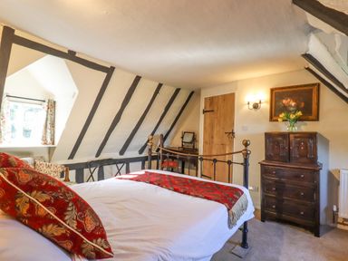 A bedroom with a bed and red pillows a window with floral curtains a dresser and a wooden door at The Abbey Cottage in Windsor Green