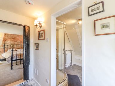 A hallway with framed pictures near a bedroom and a bathroom with a shower at The Abbey Cottage in Windsor Green