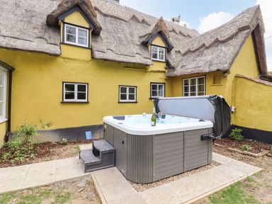 A courtyard with a hot tub and steps outside a yellow thatched cottage at The Abbey Cottage in Windsor Green