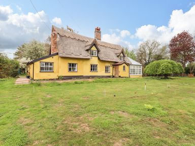 A yellow thatched cottage with a conservatory and lawn with croquet equipment at The Abbey Cottage in Windsor Green