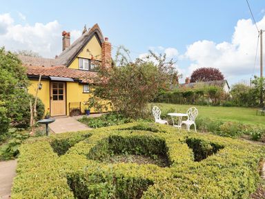 A garden with a trimmed hedge and white metal table and chairs outside a yellow cottage at The Abbey Cottage in Windsor Green