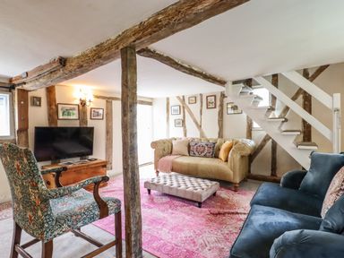 A living room with a beige sofa blue armchair patterned chair and pink rug at The Abbey Cottage in Windsor Green
