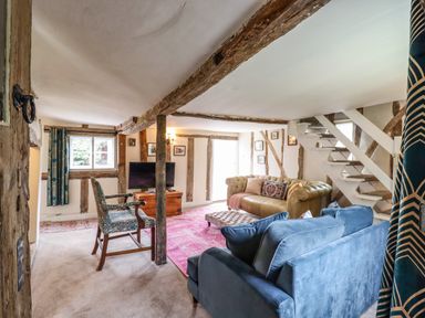 A living room with exposed wooden beams sofas armchair ottoman and a television at The Abbey Cottage in Windsor Green