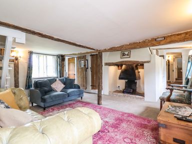 A living room with sofas a fireplace wooden beams and a pink rug at The Abbey Cottage in Windsor Green