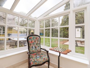 A sunroom with a floral upholstered chair and a chess table next to large windows at The Abbey Cottage in Windsor Green