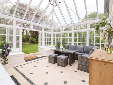 A conservatory with glass ceiling and walls a wicker sofa a table two stools and plants at The Abbey Cottage in Windsor Green