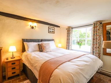 A bedroom with a bed pillows bedside lamps and floral curtains at The Abbey Cottage in Windsor Green