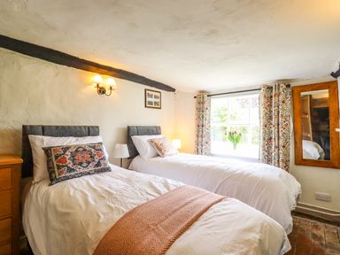 A bedroom with two single beds a window with floral curtains and a wall mirror at The Abbey Cottage in Windsor Green