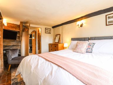 A bedroom with a bed a chair a dresser with a mirror and a television at The Abbey Cottage in Windsor Green