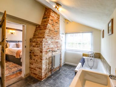 A bathroom with a bathtub sink and exposed brick wall next to a bedroom at The Abbey Cottage in Windsor Green