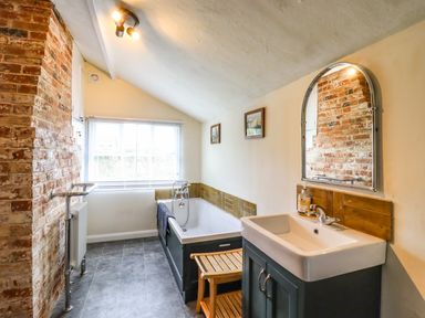 A bathroom with a bathtub sink mirror brick wall and window at The Abbey Cottage in Windsor Green