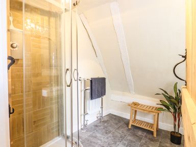 A bathroom with a glass shower enclosure a wooden bench a towel rack with a towel and a potted plant at The Abbey Cottage in Windsor Green