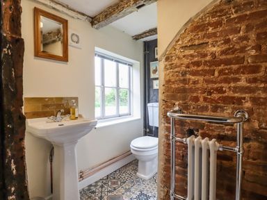 A bathroom with a pedestal sink mirror window toilet patterned floor and exposed brick wall at The Abbey Cottage in Windsor Green