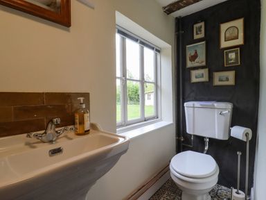 A bathroom with a sink and soap dispenser next to a window and a toilet with framed pictures on the wall at The Abbey Cottage in Windsor Green