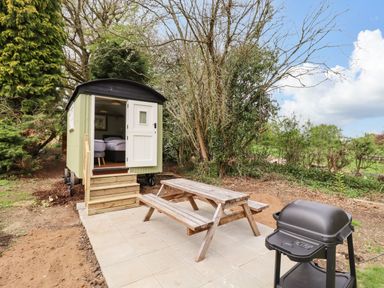 An outdoor area with a small green cabin with open door wooden picnic table and barbecue grill at The Abbey Cottage in Windsor Green