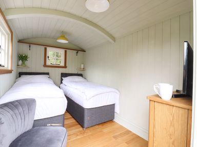 A bedroom with two single beds, a gray chair, a wooden cabinet with a TV and two white mugs, and a small window at The Abbey Cottage in Windsor Green