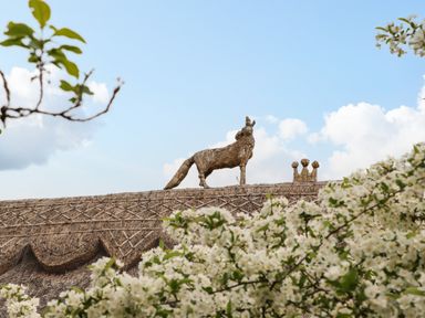 A straw sculpture of a fox and crown on a thatched roof with flowering trees in the foreground at The Abbey Cottage in Windsor Green