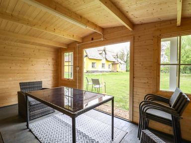 An indoor wooden room with a glass table and wicker chairs with a view of a lawn and yellow house at The Abbey Cottage in Windsor Green