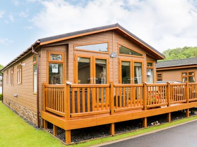 A wooden lodge with a deck and railings on a grassy area at Hafan Lodge 85 Wisemans Bridge near Saundersfoot