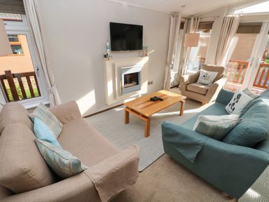 A living room with beige and blue sofas a wooden coffee table a wall-mounted TV and a fireplace at Hafan Lodge 85 Wisemans Bridge near Saundersfoot
