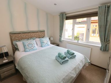A bedroom with a double bed with pillows and rolled towels near a window with curtains at Hafan Lodge 85 Wisemans Bridge near Saundersfoot