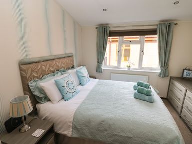 A bedroom with a bed with pillows and towels next to a window with curtains at Hafan Lodge 85 Wisemans Bridge near Saundersfoot
