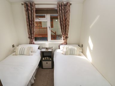 A bedroom with two single beds a small nightstand and a window with curtains at Hafan Lodge 85 Wisemans Bridge near Saundersfoot